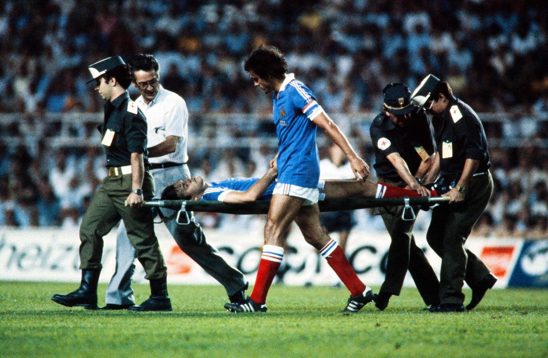 Frankrigs anfører, Michel Platini, holder den franske forsvarsspiller Patrick Battiston (på båren) i hånden. Han er netop blevet skadet under VM-opgøret mellem Vesttyskland og Frankrig den 8. juli 1982 i Sevilla.
